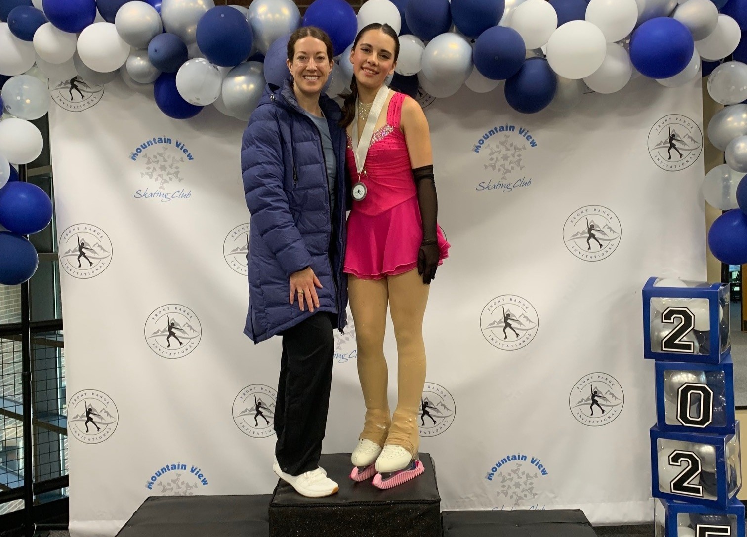 Haley Madsen poses at the Greeley Ice Haus on a podium with her coach, Sarah Bott.