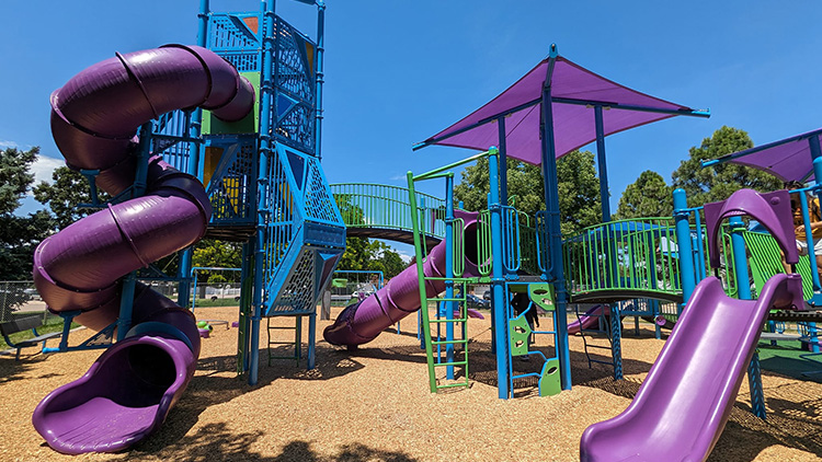 A purple playground with a large spiral slide and tall blue climbing structure and trees in the background.