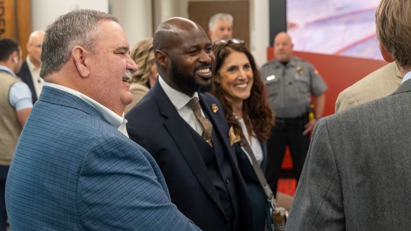 Greeley Mayor John Gates and City Manager Raymond Lee stand side-by-side smiling while talking to a group of people.