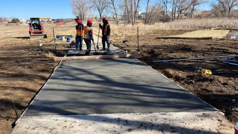 Three workers pour concrete into a section of a walking path.