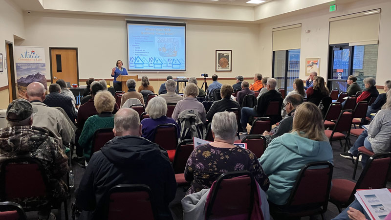 Woman at a podium gives a presentation to a full room of people