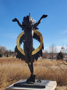 Bronze sculpture of Native American in crucifix form with a bright sash arching behind.